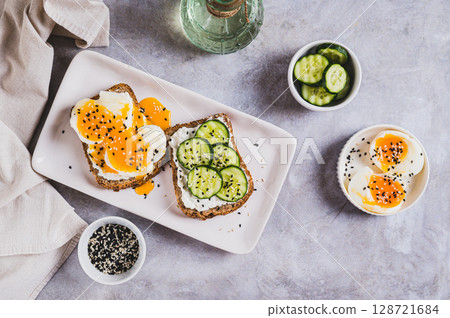 Open sandwiches with ricotta, cucumber and soft-boiled egg on a plate on a table top view Open sandwiches with ricotta, cucumber and soft-boiled egg on a plate on a table top view 128721684