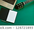 A textured background featuring a laptop, a blank notebook, a pen, and an acoustic guitar. Ideal for online guitar  128721893