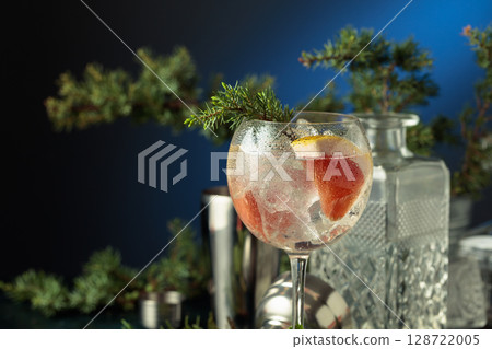 Cocktail gin and tonic with ice and pink grapefruit slices in wet glass on a dark blue background. 128722005