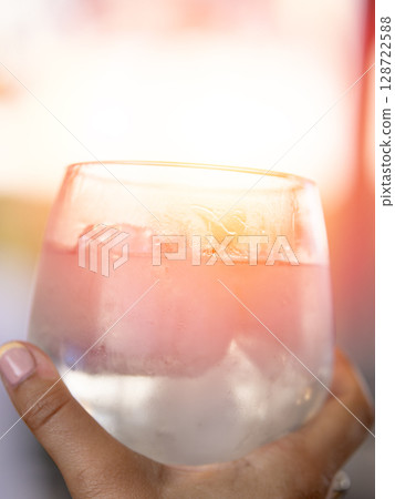 Frosted cocktail glass with pink hue and ice held by hand in warm light Frosted cocktail glass with pink hue and ice held by hand in warm light 128722588