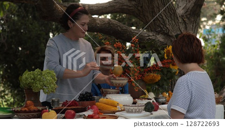 Celebration of Thanksgiving dinner outdoors surrounded by nature filled with tables of vibrant food and joyful family, showcasing the warmth and togetherness shared during festive gatherings 128722693