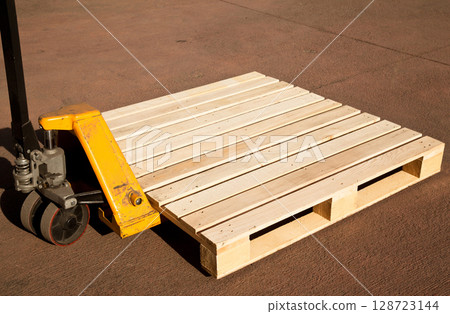 Empty wooden pine pallet with a pallet truck or transpallet in front of a warehouse, logistics and industrial transportation 128723144
