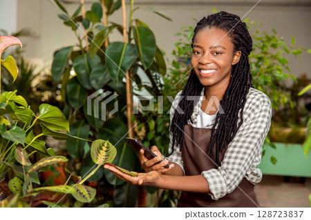 Flower shop assistant making pictures of plant and smiling Flower shop assistant making pictures of plant and smiling 128723837