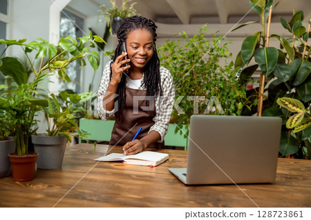 Cute smiling flower shop assistant taking orders by phone 128723861