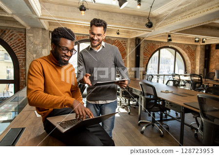 Colleagues working together in the office and looking contented Colleagues working together in the office and looking contented 128723953