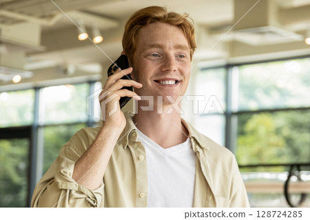 Smiling young man looking excited while talking on the phone Smiling young man looking excited while talking on the phone 128724285