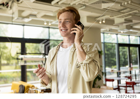 Ginger young man in cafe talking on the phone and looking enjoyed Ginger young man in cafe talking on the phone and looking enjoyed 128724295