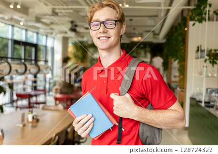 Smiling young guy with books in hands looking positive and joyful 128724322