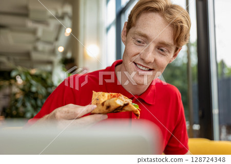 Young ginger man eating pizza and looking enjoyed 128724348