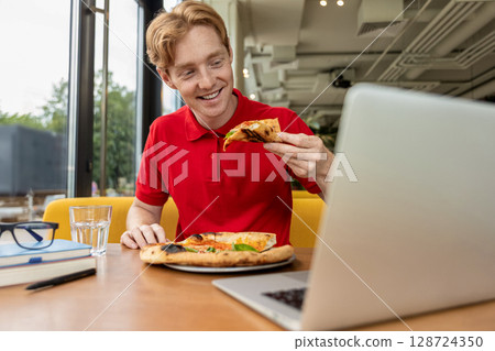 Young ginger man eating pizza and looking enjoyed 128724350