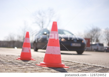 Two orange cones are on the ground in front of a car 128724452