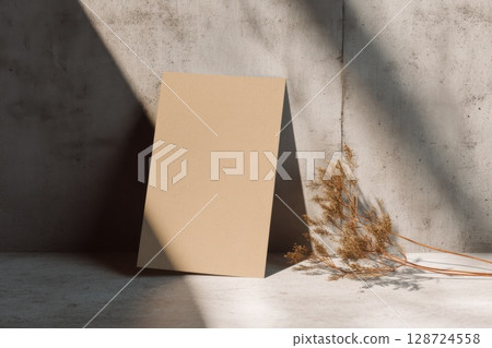 Vertical cardboard mockup leans against a concrete wall with dry plant shadows, creating a raw minimal scene ideal for eco branding or stationery design 128724558
