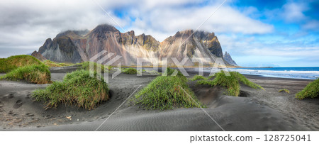 Astonishing sunny day and gorgeous rippled black sand beach with dunes and green grass on Stokksnes cape in Iceland. Astonishing sunny day and gorgeous rippled black sand beach with dunes and green grass on Stokksnes cape in Iceland. 128725041