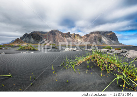 Amazing sunny day and gorgeous rippled black sand beach with dunes and green grass on Stokksnes cape in Iceland. 128725042