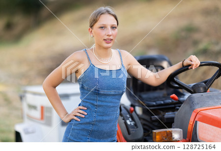 Young woman posing near tractor in countryside Young woman posing near tractor in countryside 128725164