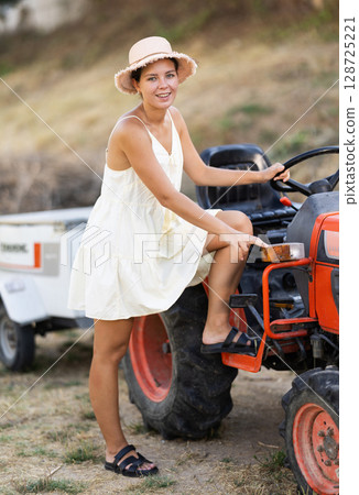Girl in summer sundress near tractor Girl in summer sundress near tractor 128725221