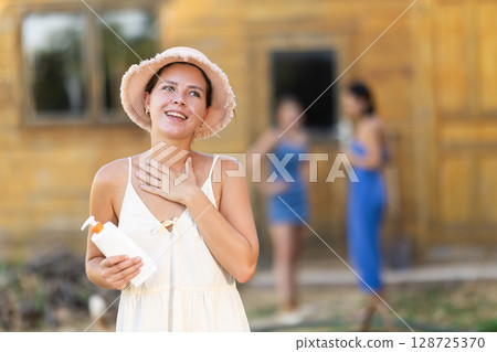 Young woman applying sunscreen outside country house 128725370