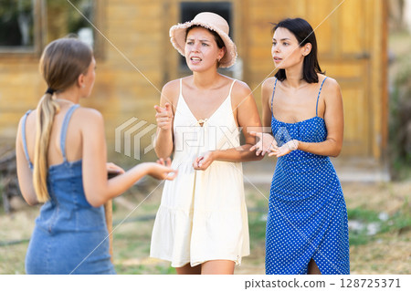 Three young women neighbors quarrel and swear in rural yard 128725371