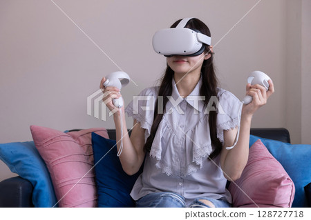 一位日本女性在家中客廳戴著 VR 眼鏡享受虛擬現實 一位日本女性在家中客廳戴著 VR 眼鏡享受虛擬現實 128727718