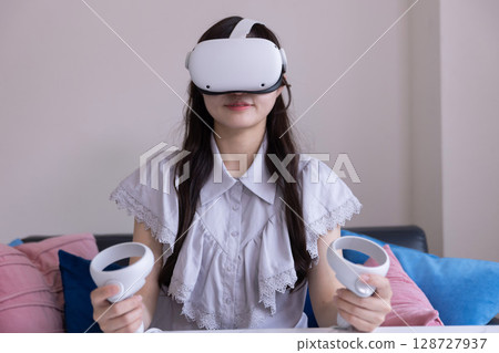 一位日本女性在家中客廳戴著 VR 眼鏡享受虛擬現實 一位日本女性在家中客廳戴著 VR 眼鏡享受虛擬現實 128727937