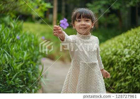 happy toddler girl in white dress with Ruellia simplex or Mexican petunia flower in garden 128727961