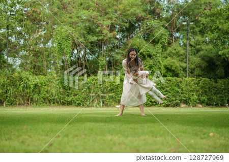 mother and toddler girl playing circling around on grass field at park 128727969