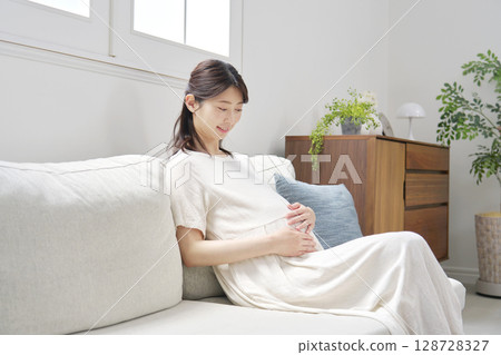 Pregnant woman sitting on the sofa and touching her stomach 128728327