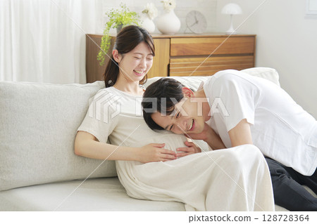 Husband putting his ear to his pregnant wife's belly 128728364