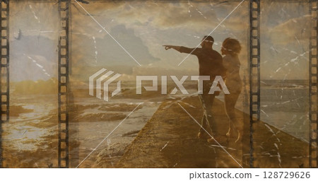 Pointing couple gazing toward horizon on jetty at sunset, with filmstrip borders, copy space Pointing couple gazing toward horizon on jetty at sunset, with filmstrip borders, copy space 128729626