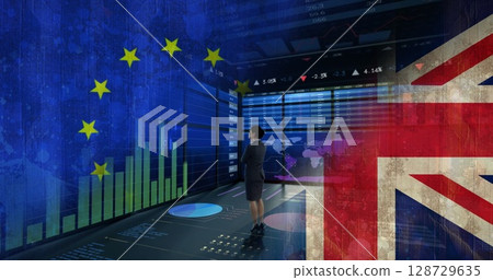 Standing professional in skirt suit and heels observing data room, with EU and UK flag graphics 128729635