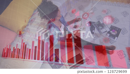 Woman reviewing printed charts in living room, with laptop smartphone sofa data overlay, copy space 128729699