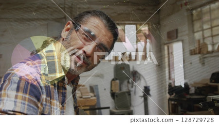 Holding wooden plank, working at woodshop bench, wearing protective glasses and plaid shirt 128729728