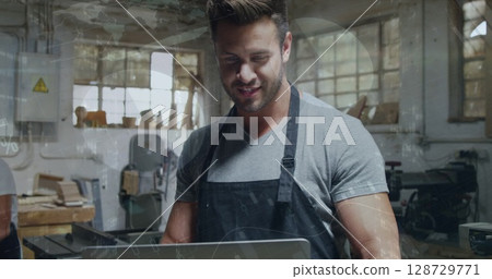 Examining craftsperson using laptop at woodworking bench in workshop, with band saw and drill press Examining craftsperson using laptop at woodworking bench in workshop, with band saw and drill press 128729771