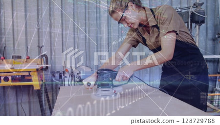 Sanding woman craftsperson using orbital sander on board in workshop, with binary graphics overlay 128729788