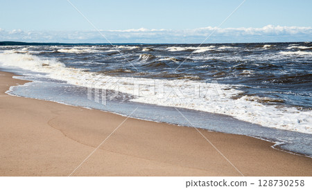 Waves Crashing on a Sandy Beach Shoreline Under a Bright Blue Summer Sky Waves Crashing on a Sandy Beach Shoreline Under a Bright Blue Summer Sky 128730258