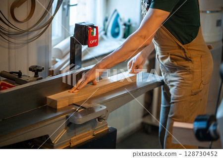 Carpenter use electric planer removing excess wood with saw on woodworking machine. Wood shaping 128730452