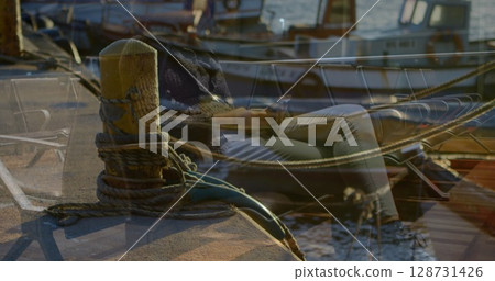 Sitting woman in navy sweater and light pants checking phone on marina dock, with coiled ropes 128731426