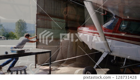Pushing man in jeans opening hangar door at hangar entrance, with propeller plane, piano overlay Pushing man in jeans opening hangar door at hangar entrance, with propeller plane, piano overlay 128731428
