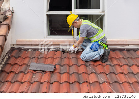 Construction worker painting sealant adhesive to fix crack of the old tile roof. 128732146