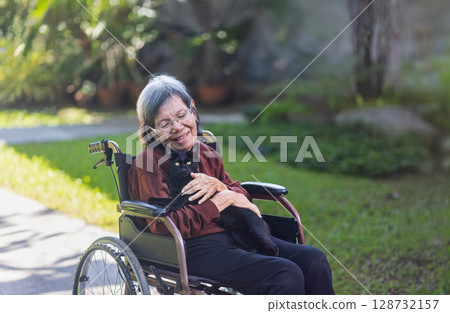 Elderly asian woman holding baby black cat in backyard. Elderly asian woman holding baby black cat in backyard. 128732157