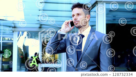 Talking man in dark suit and tie holding smartphone at sliding glass entrance, with euro overlays 128732334