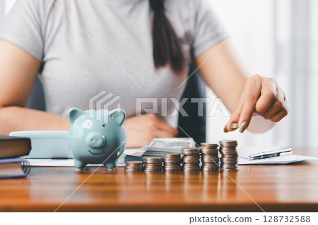 Businesswoman saving money with piggy bank and coins on desk, financial planning and investment concept. Young Asian woman making stack of coin. invest save finance concept, saving money, investment 128732588