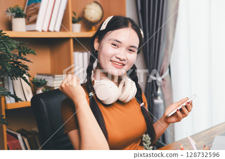 Asian girl doing homework and studying at home. woman using laptop at desk write notes watching webinar, study online, look at learn web class or having virtual call meeting remote working from home. 128732596