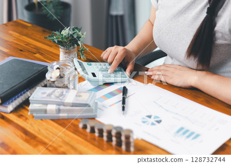Young Asian woman making stack of coin. invest save finance concept, saving money, investment. dollar bills on table with pile of coins and banks calculator, money to save and invest to make income. 128732744