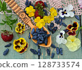 Garden still life with beautiful flowers of pansy with ripe honeysuckle berry in the spoon on the table. Summer botanical and farming background with gardening objects, vintage home concept Garden still life with beautiful flowers of pansy with ripe honeysuckle berry in the spoon on the table. Summer botanical and farming background with gardening objects, vintage home concept 128733574