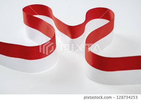 The striped red and white ribbon of the Indonesian flag on a white background. Concept of Indonesian Independence Day or Kemerdekaan 128734253