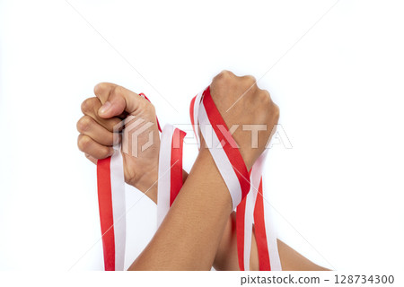 Human hand holding the Indonesian ribbon flag to celebrate Indonesia Independence Day isolated over a white background. Concept of Kemerdekaan Human hand holding the Indonesian ribbon flag to celebrate Indonesia Independence Day isolated over a white background. Concept of Kemerdekaan 128734300