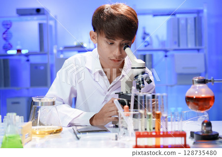 Young scientist looking through a microscope in the laboratory. Young scientist looking through a microscope in the laboratory. 128735480