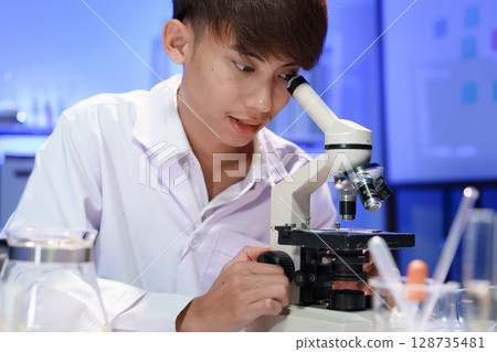 Young scientist looking through a microscope in the laboratory. 128735481