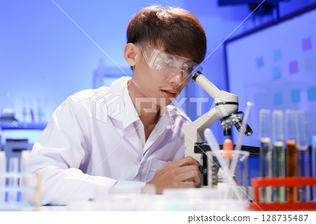 Young scientist looking through a microscope in the laboratory. Young scientist looking through a microscope in the laboratory. 128735487
